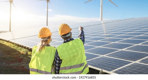 People Working For Alternative Energy Farm - Wind Turbine Power Generators Process And Solar Panels - Focus On Helmets