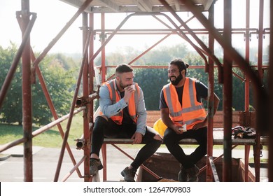 People Working In Construction Site. Men At Work In New Housing Project. Team Of Happy Workers Laughing, Talking And Eating Snack During Lunch Break