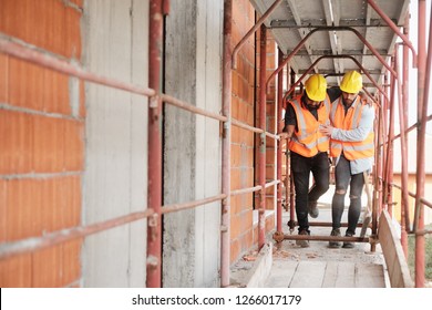 People Working In Construction Site. Young Men At Work In New House Inside Apartment Building. Latino Manual Worker Helping Injured Co-worker After Accident On Duty