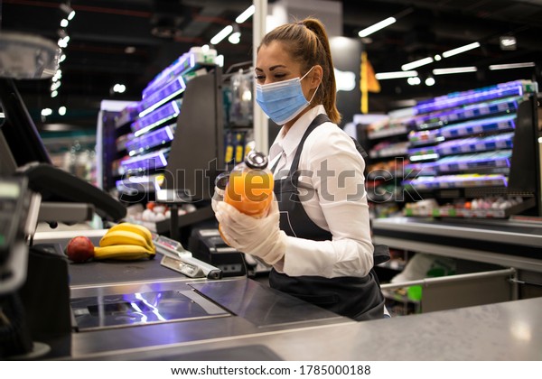 People working during global virus pandemic.\
Cashier at supermarket wearing mask and gloves fully protected\
against corona virus.