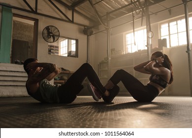 People Working Out In Gym. Fit Man And Woman Doing Sit Ups Together.