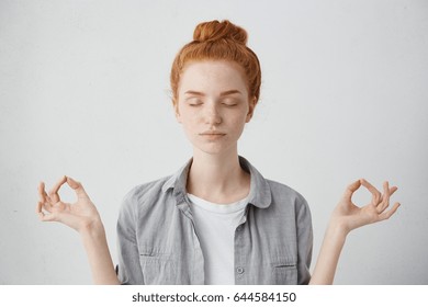 People, yoga and healthy lifestyle concept. Portrait of gorgeous young redhead woman keeping eyes closed while meditating indoors, practicing piece of mind, keeping fingers in mudra gesture