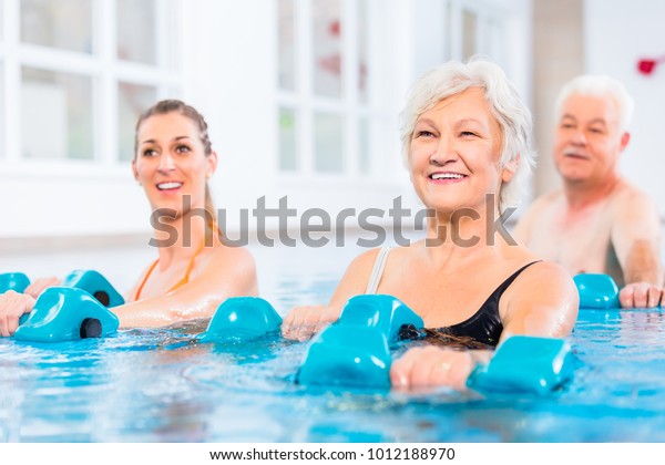 People young and senior in water gymnastics\
physiotherapy with\
dumbbells