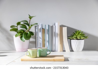 Peperomia magnoliifolia in a pink plastic pot, echeveria in a ceramic pot, a stack of books is on the bookshelf. Interior of a teenager's room. Green and light green coffee cups on small wooden board - Shutterstock ID 2157313043