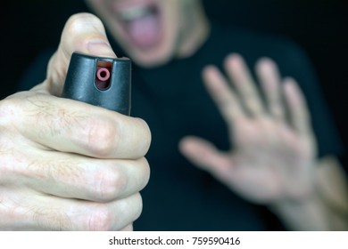 pepper gas in the hand of a young man in a black jacket screams CS spray self-defense Tear gas concept, close up, selective focus , blurred dark background