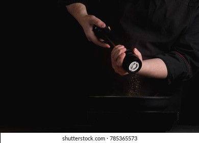 Pepper Mill In Chef Hands On Black Background.