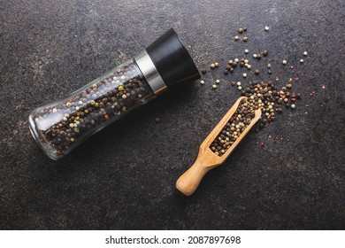 Pepper mill and whole pepper in wooden scoop on black table. Top view. - Powered by Shutterstock