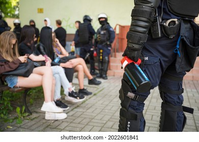 Pepper spray manual(with inscription in Polish "Police") is held by a policeman in the background young people and other policemen.