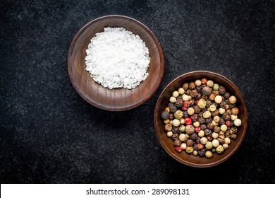 peppercorns and sea salt in a wooden bowl on a dark background