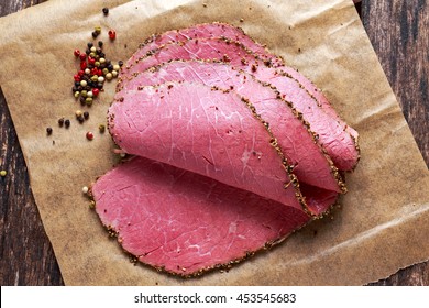 Peppered roast beef pastrami slices on paper with grains of coloured pepper.