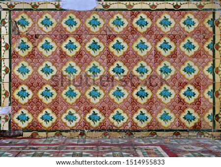 Peranakan tile mosaic as typically found on traditional Chinese shop houses, with turquoise blue flowers on a scalloped red and maroon background and geometric floor tiles in the foreground. 