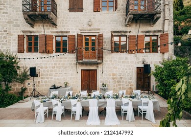 Perast, Montenegro - 04.04.19: Wedding dinner table reception. Grey long rectangular table and fourteen chairs outside the old villa. Sunset light, mountains are reflected in glass