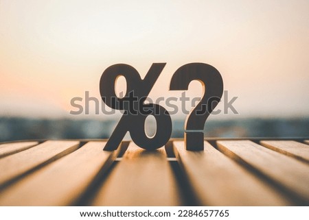 Percentage and question mark on wood table in blur urban background, raising or lowering Fed interest rates to correct inflation concepts.