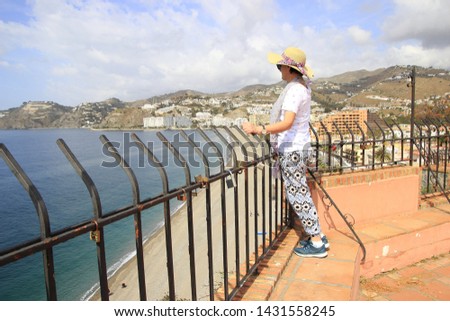 Perched by the sea of mature woman with hat and pants, tourist woman with pamela, observing the landscape, the beach and the sea from a viewpoint of Almuñecar in the Peñones de San Cristóbal, Malaga,