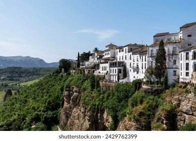 Perched on a dramatic cliff side, white buildings of a historic town Ronda overlook lush green valleys, marrying nature's grandeur with human history.