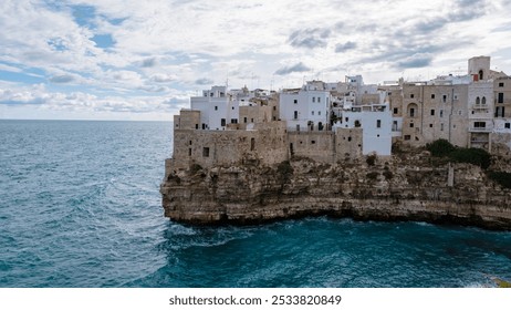 Perched on a rocky cliff, the picturesque village of Puglia boasts whitewashed buildings overlooking the shimmering blue sea, as dramatic clouds loom overhead, Polignano a Mare Italy  - Powered by Shutterstock