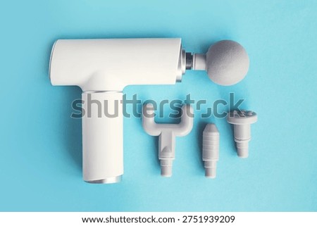 Percussion massage gun with multiple interchangeable attachment heads on blue background. Modern electric device for muscle recovery, physiotherapy, sports rehabilitation and deep tissue massage after workout.