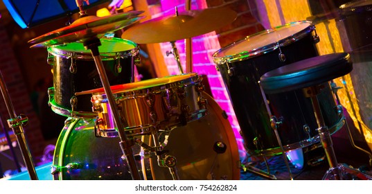 Percussion Musical Instruments. Beautifu Music Background. Drum Set On The Stage In Multicolored Rays Of Concert Light Closeup With Selective Focus. Colorful Wide Screen Wallpaper Or Web Banner