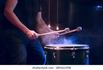 The percussionist plays with sticks on the floor tom on under studio lighting.. Concert and performance concept.