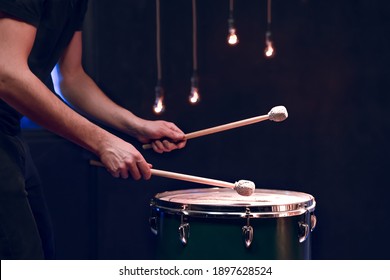 The percussionist plays with sticks on the floor tom in a dark room with beautiful lighting. Concert and performance concept.