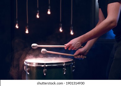 The percussionist plays with sticks on the floor tom in a dark room with beautiful lighting. Concert and performance concept.