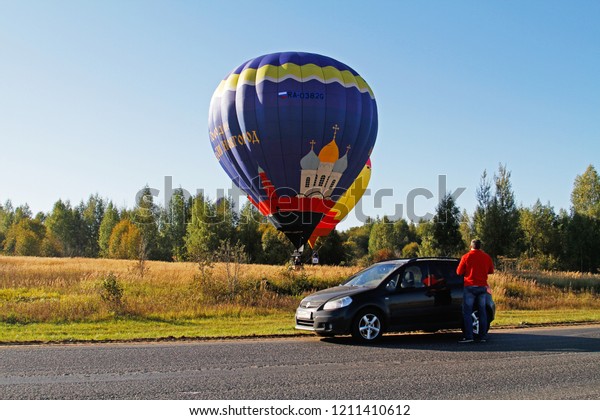 Pereslavl-Zalessky, Russia - September\
23, 2017: Man near the car watching as two hot air balloons land on\
the field at the festival of aeronautics in\
Pereslavl-Zalessky