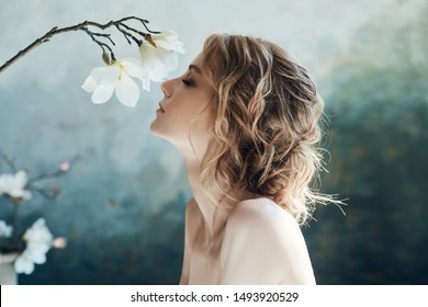 Perfect bride, portrait of a girl in a long white dress. Beautiful hair and clean delicate skin. Wedding hairstyle blonde woman. Girl with a white flower in her hands