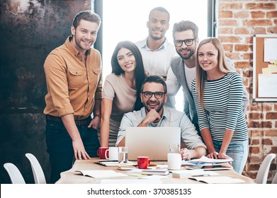 Perfect Creative Team. Group Of Six Cheerful Young People Looking At Camera With Smile While Leaning To The Table In Office