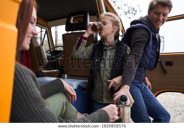 Perfect day together. Pleasant man pours hot tea from\
a thermos for his charming wife. She looks gratefully at the cup of\
aromatic drink. Their daughter stands between them and finishes\
drinking her