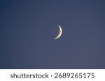 A perfect, delicate crescent moon glowing in a clear, deep blue sky at twilight. A beautiful, minimalist astrophotography shot with plenty of serene copy space