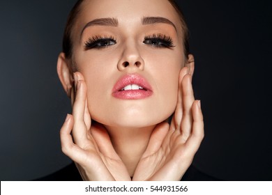 Perfect Face Makeup. Closeup Portrait Of Beautiful Sexy Woman With Professional Makeup Touching Her Smooth Soft Healthy Facial Skin. Glamorous Female Model With Long Black Eyelashes. High Resolution