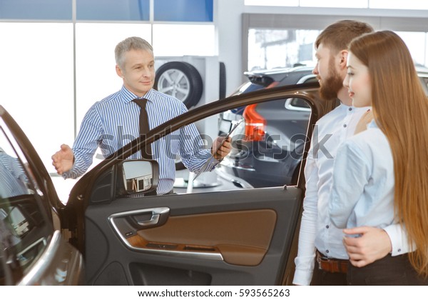 Perfect for the family. Beautiful young couple\
buying a new car at the dealership cheerful mature car salesman\
showing his customers a car profession occupation family\
relationship love travel\
auto