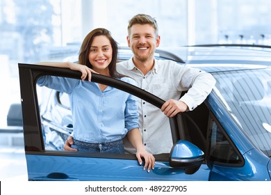 Perfect Family Car. Shot Of A Beautiful Happy Couple Posing Together Behind An Open Door Of A New Car They Just Bought At The Dealership Smiling To The Camera Joyfully