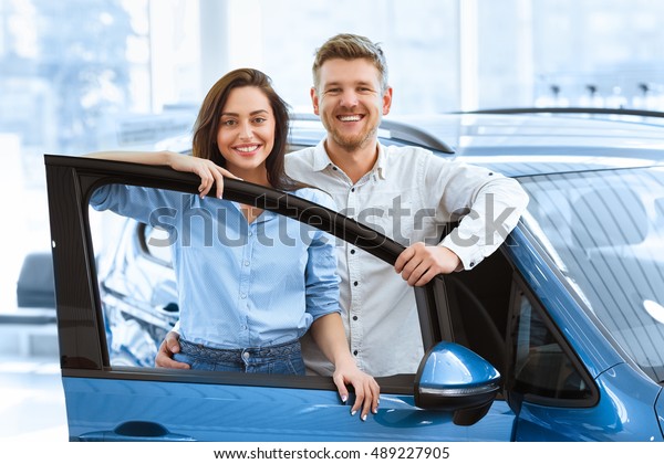 Perfect family car. Shot\
of a beautiful happy couple posing together behind an open door of\
a new car they just bought at the dealership smiling to the camera\
joyfully
