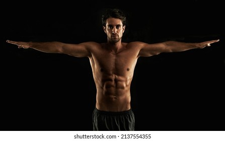 Perfect form. Handsome topless man raising his arms to his side - Isolated on black.