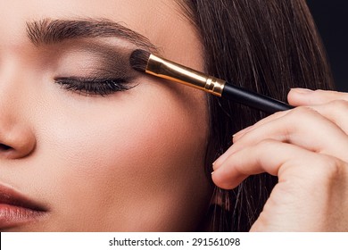 For Perfect Glance. Close-up Of Young Woman Applying Eye Shadow While Standing Against Black Background