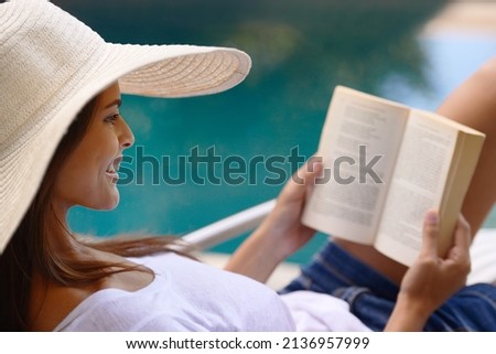 The perfect holiday read. Shot of a young woman reading a book by the poolside.