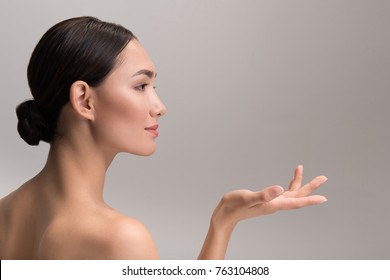 Perfect Skincare And Beauty Concept. Side View Profile Of Positive Attractive Young Asian Woman Is Holding Palm Up And Looking Ahead With Slight Smile. Isolated With Copy Space In The Right Side