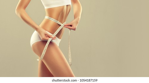  Perfect slim toned young body of the girl . An example of sports , fitness or plastic surgery and aesthetic cosmetology.Woman measuring her waist over white background - Shutterstock ID 1054187159