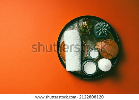 Perfect Spa still life with a natural cosmetic products, candles and flower on a copper plate on red background with copy space.