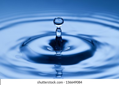 Perfect spherical droplet of water suspended midair above the surface of the liquid with radiating ripples