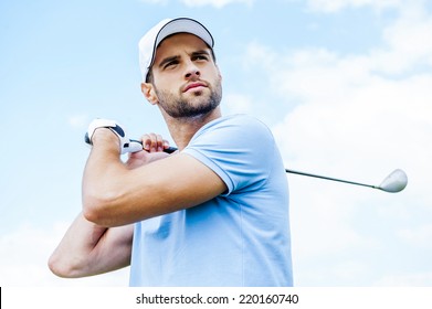 Perfect strike. Low angle view of young golfer swinging his driver and looking away with blue sky as background - Powered by Shutterstock