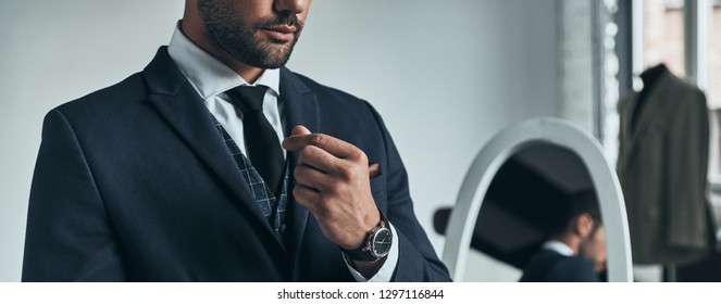 Perfect style. Close up of young man in full suit adjusting sleeve while standing indoors