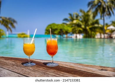 Perfect summer beach resort, poolside with two colorful cocktails. Tropical swimming pool, exotic summer vacation. Chairs, umbrella blurred palm tree leaves, amazing landscape. Freedom relax holiday