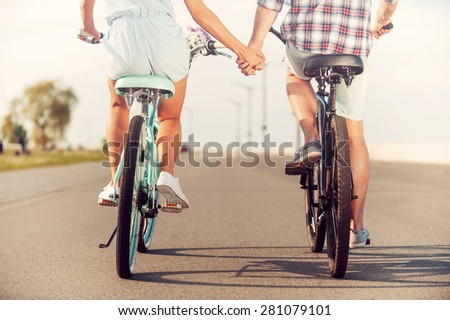 The perfect summer date. Rear view of young couple holding hands while riding on bicycles along the road