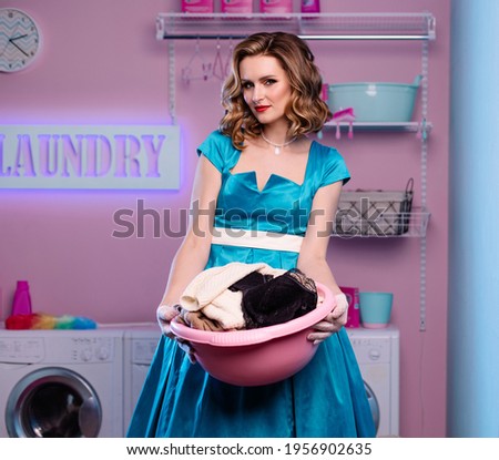 perfect tradwife wife in the laundry room with dirty linen. A basin with dirty clothes in his hands. A housewife in a good mood is working on the house. Housekeeper in the laundry positive emotions. 