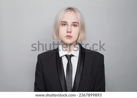 Perfect young adult business woman with short straight blonde haircut wearing black male style suit with tie