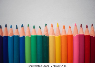 A perfectly aligned row of sharpened colored pencils, showcasing a spectrum of bright hues against a clean white backdrop, ready for artistic creation.