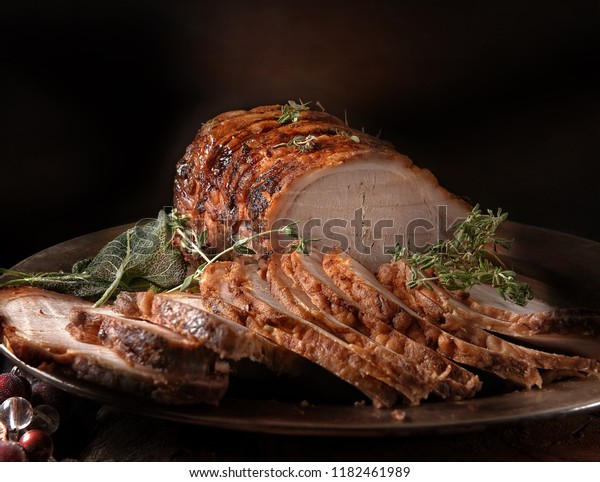 A perfectly\
oven roasted prime pork joint carved and ready to serve with thyme\
and sage herbs. Shot against a dark rustic background with generous\
accommodation for copy space.