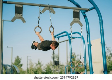 Perfectly parallel to the ground, a man confidently executes an iron cross on rings in a bright outdoor setting.